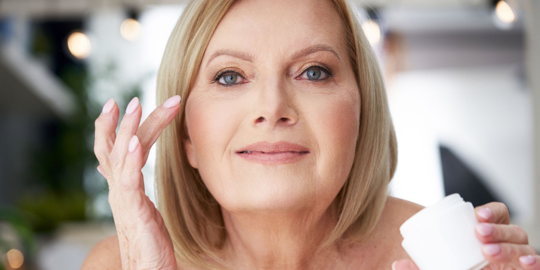 Femme d'une cinquantaine d'années se préparant à appliquer de la crème sur son visage, illustrant la beauté après 50 ans.