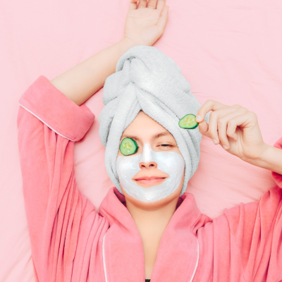 Femme souriante en peignoir avec un masque hydratant sur le visage et une serviette sur la tête