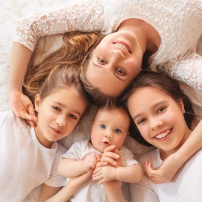 Une mère et ses trois enfants, tous vêtus de blanc, allongés en cercle et souriant à la caméra, incarnant l'harmonie et l'amour familial