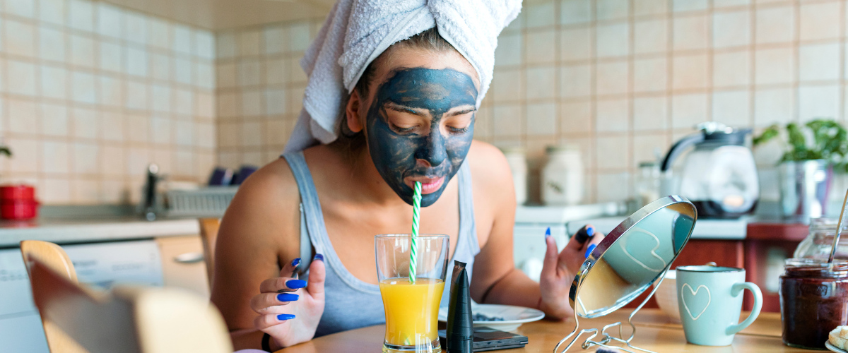 Une femme avec un masque de beauté noir profitant d'un moment de bien-être matinal tout en buvant un jus d'orange qui fait sa routine matinale